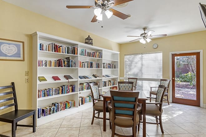 A cozy reading room with bookshelves, a table, and chairs under ceiling fans.