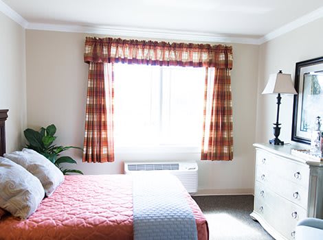 A cozy bedroom with a window, dressed bed, and decorative curtains.