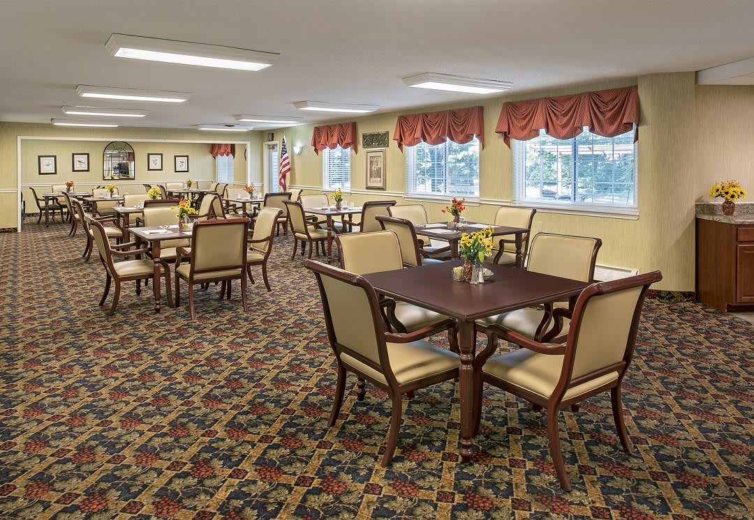 A spacious and elegant dining room with neatly arranged tables and chairs, featuring patterned carpet and decorative curtains.