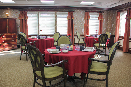 A cozy dining area featuring round tables with red tablecloths and comfortable chairs, illuminated by natural light.
