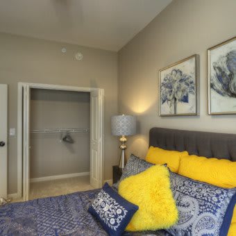A cozy bedroom with a stylish bed adorned with yellow and blue pillows, complemented by artwork on the wall and a lamp beside the bed.
