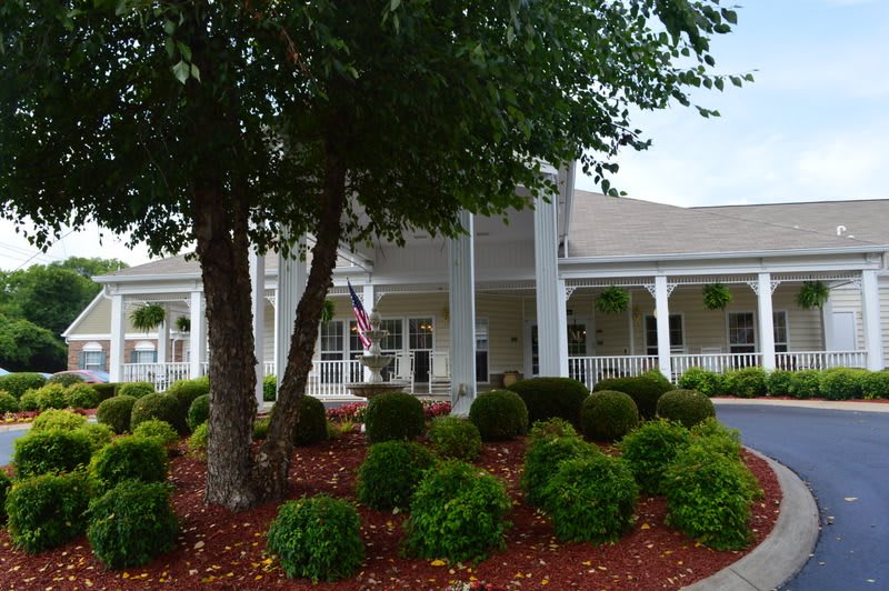 A front view of a building with a landscaped garden featuring trees and bushes.