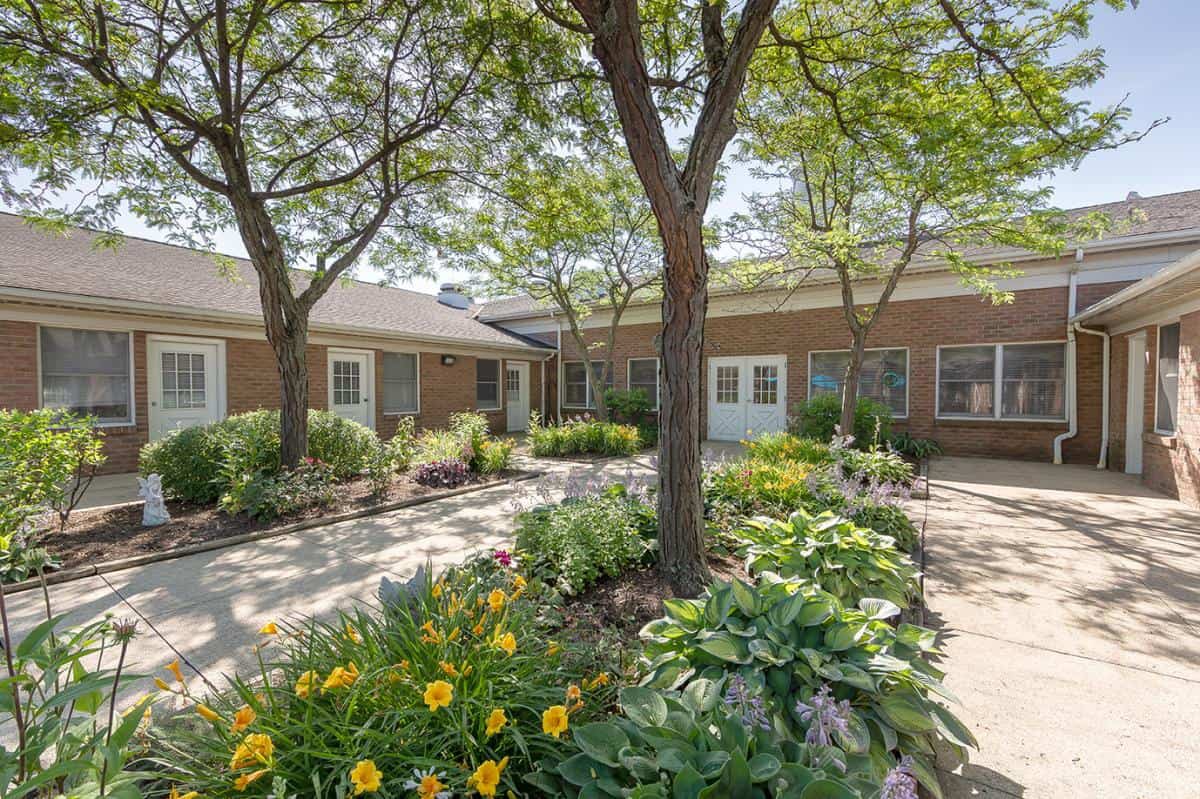 A peaceful courtyard garden with trees and flowers next to a brick building.