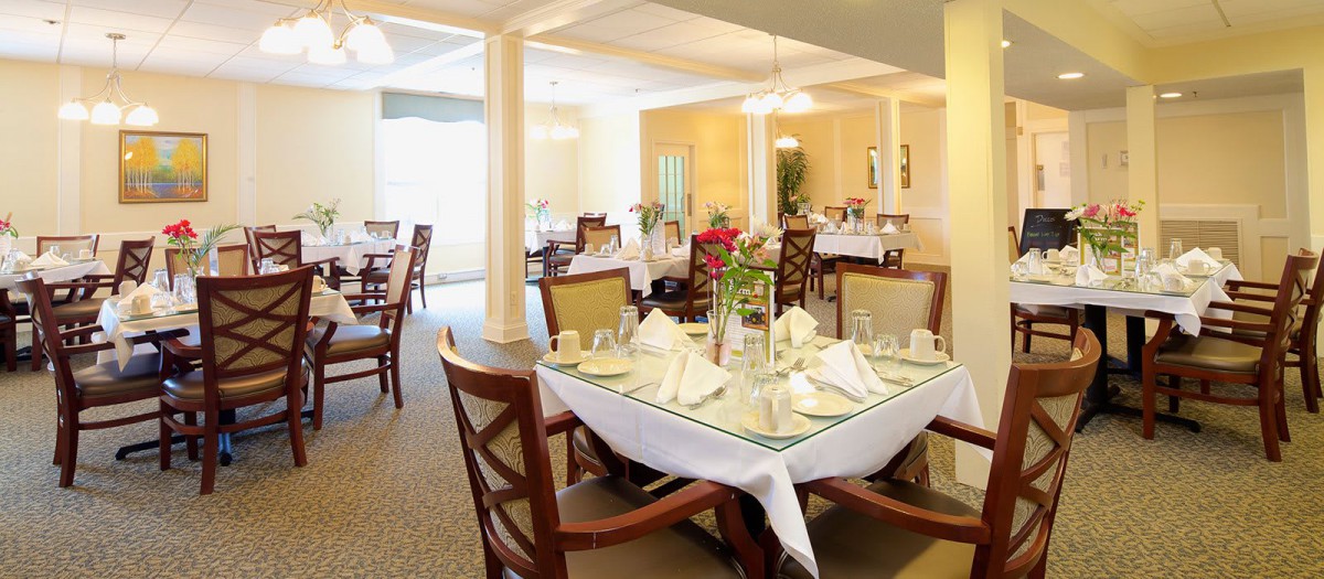 A well-lit dining room with neatly arranged tables and chairs, featuring elegant table settings.