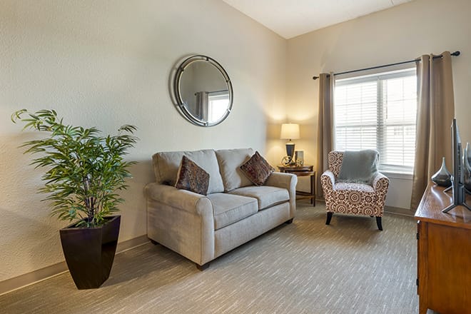 A cozy living room with a sofa, armchair, mirror, and decor elements such as a plant and lamp.