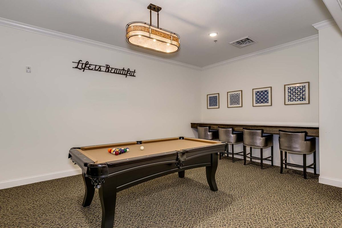 A cozy game room featuring a billiards table, stylish pendant lighting, and comfortable seating along a bar counter.