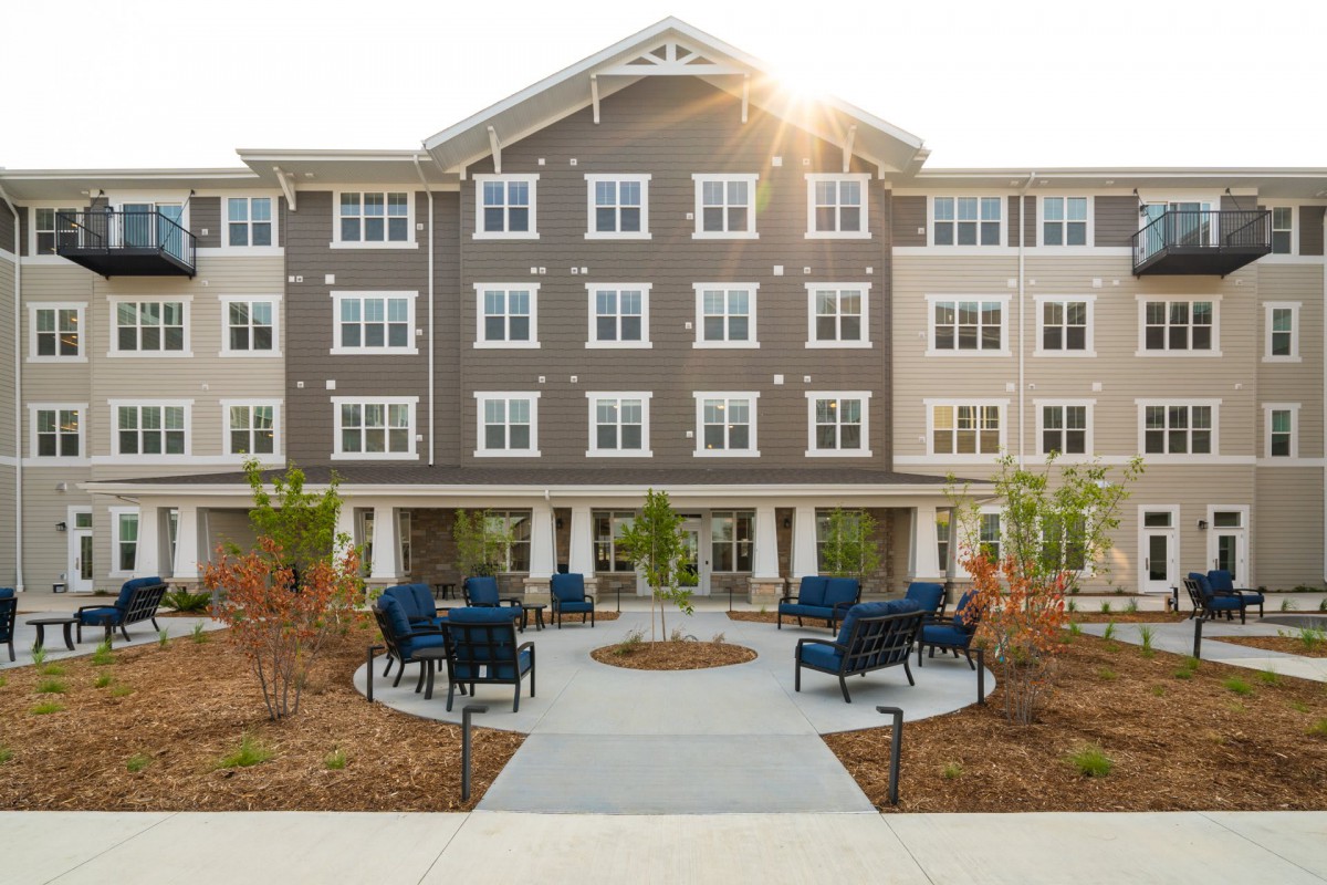 A modern residential apartment building with a landscaped courtyard featuring seating areas and pathways.