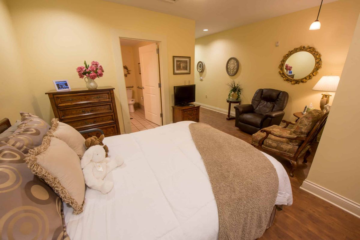 A cozy bedroom featuring a bed, armchair, dresser, and television with warm lighting.