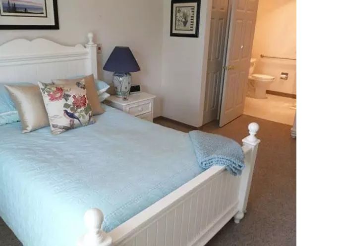 A cozy bedroom with a light blue bedspread and floral pillow, featuring a bedside table and lamp.