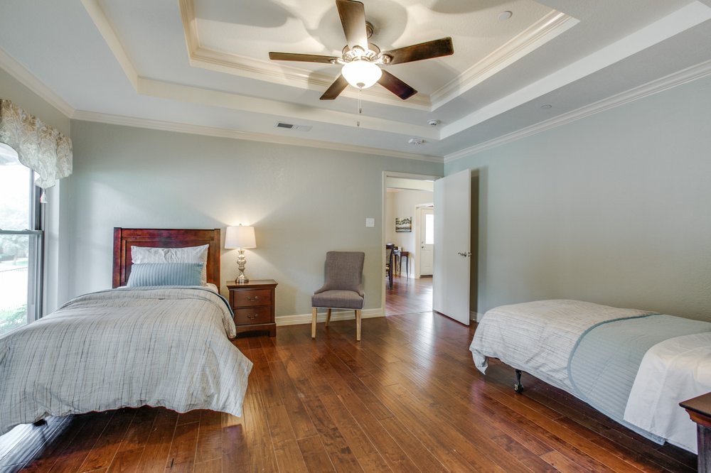 A spacious bedroom with two beds, featuring wooden flooring and a ceiling fan.