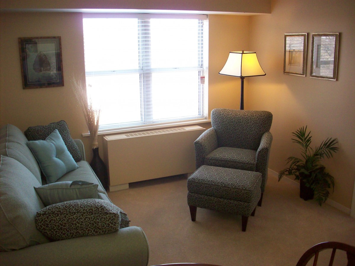 A cozy living room with a sofa, armchair, and lamp by the window.