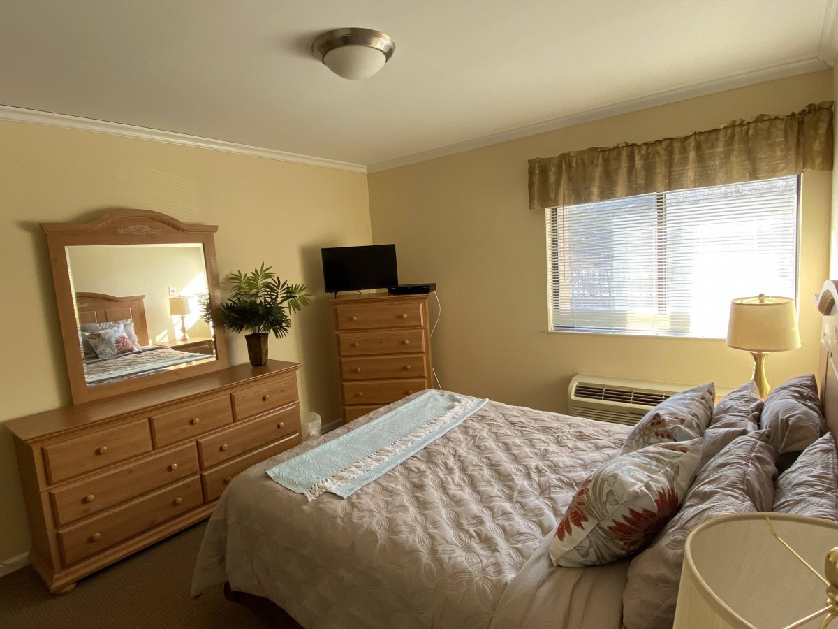 A cozy bedroom with a neatly made bed, wooden furniture, and natural light streaming through the window.