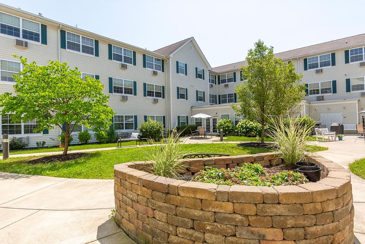 A three-story apartment building with a landscaped courtyard featuring a brick planter and greenery.