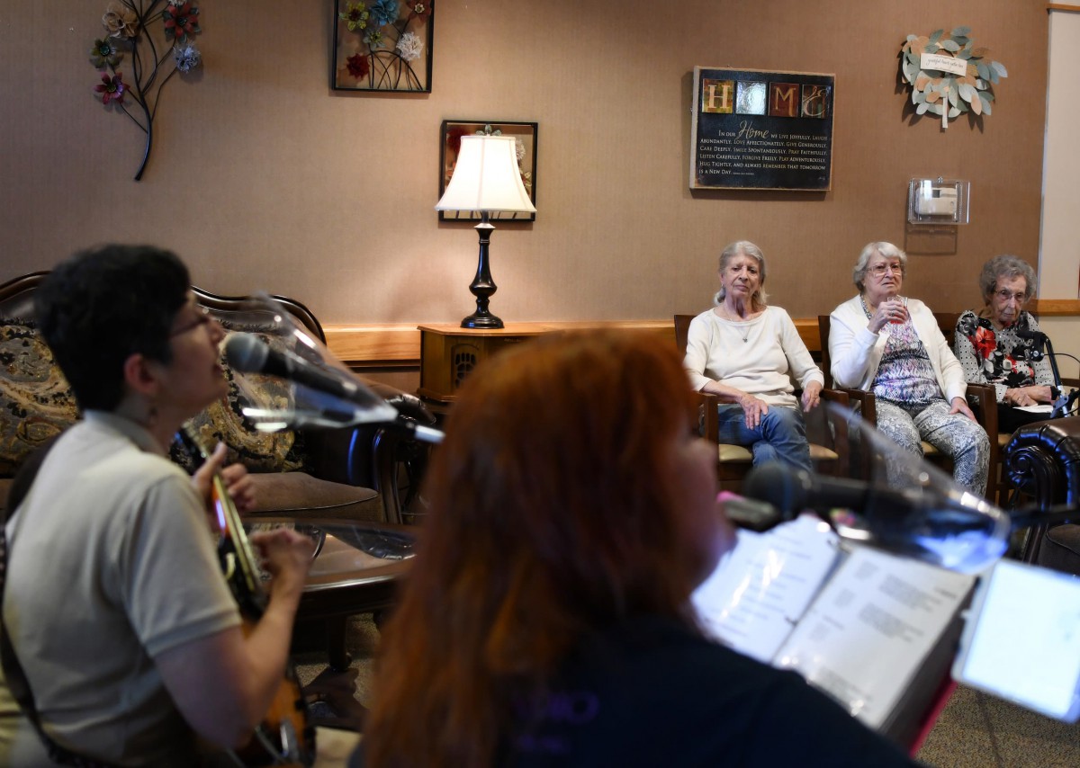 A group of people engaged in a discussion indoors, with a lamp providing light to the room.