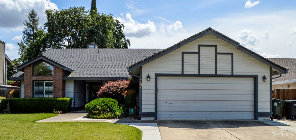 A suburban house with a garage and well-maintained front yard under a partly cloudy sky.
