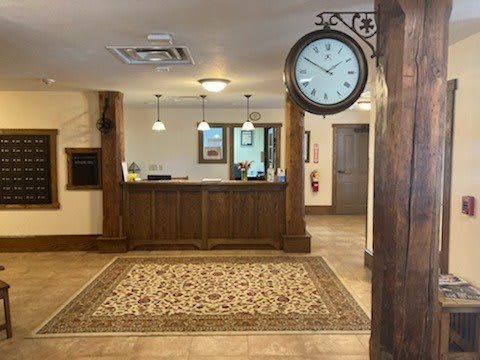 A hotel lobby with a reception desk, ornate rug, and a wall-mounted clock.