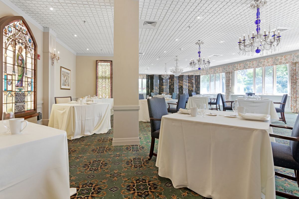 An elegant banquet hall with white tablecloths and chandeliers, set up for an event.