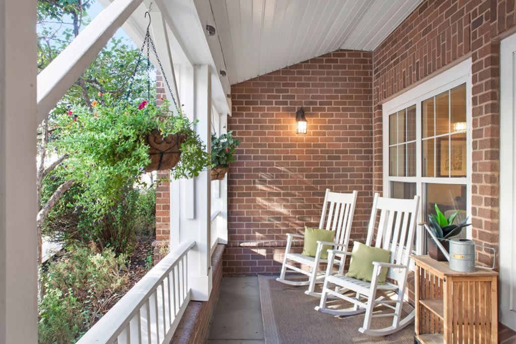 A cozy porch with white rocking chairs and hanging plants against a brick wall.