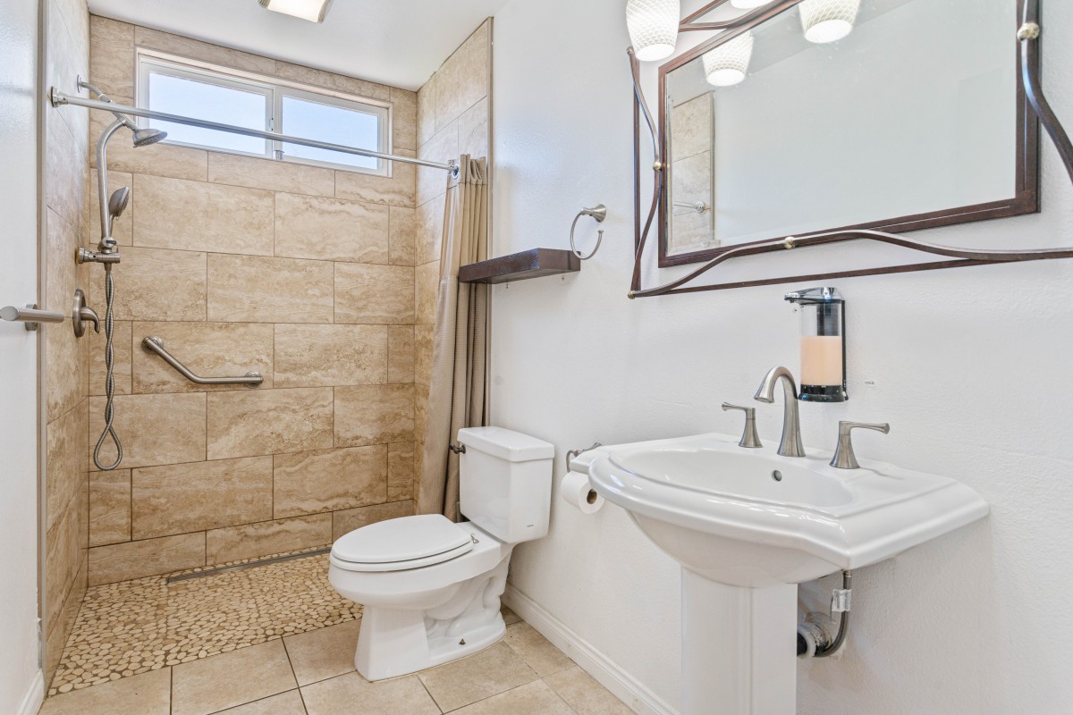A modern bathroom with a spacious walk-in shower, pedestal sink, and tiled flooring.