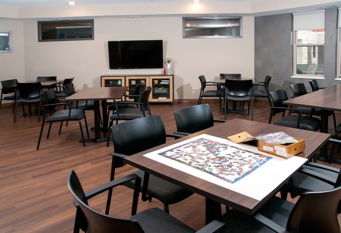 A cozy game room featuring tables, chairs, a television, and a puzzle in progress.
