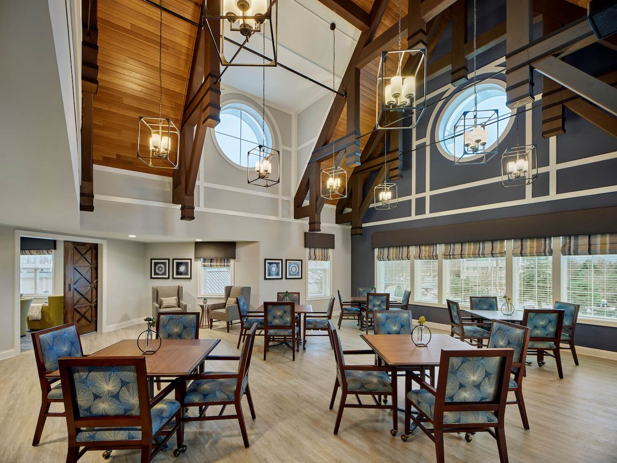 A spacious dining area with high ceilings, stylish lighting, large windows, and neatly arranged tables and chairs.
