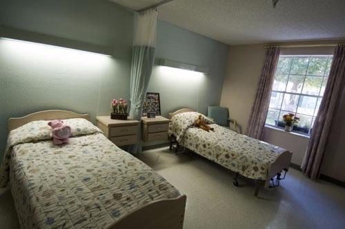 A shared nursing home room with two twin beds, light floral bedding, and a window providing natural light.