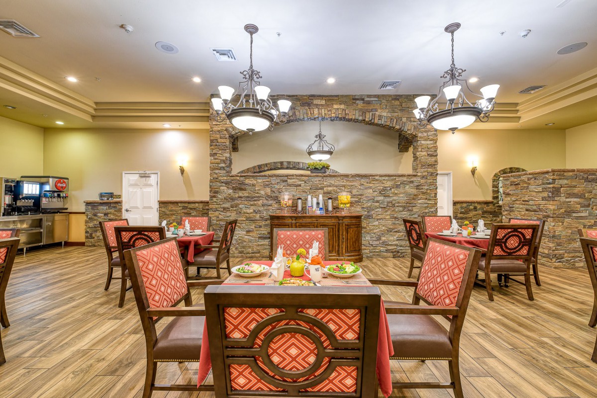 A warmly lit dining area with elegant chandeliers, stone walls, and neatly arranged tables.