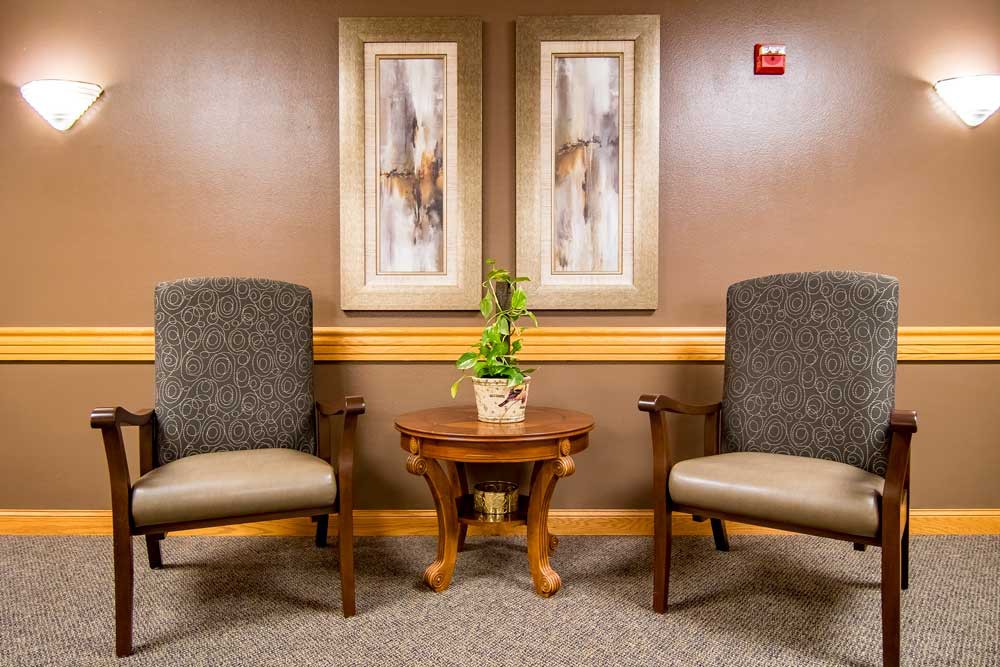 A waiting room with two chairs, a small wooden table with a plant, and abstract artwork on the wall.