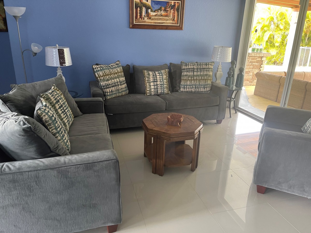 A cozy living room with blue walls, featuring comfortable sofas, patterned cushions, a round wooden coffee table, and decorative lamps.