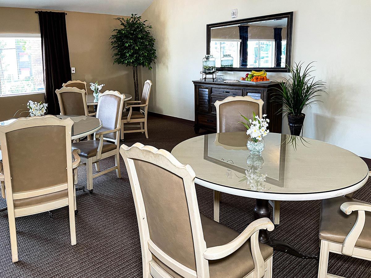 A well-furnished dining room with elegant tables and chairs, accented by indoor plants and a large mirror.