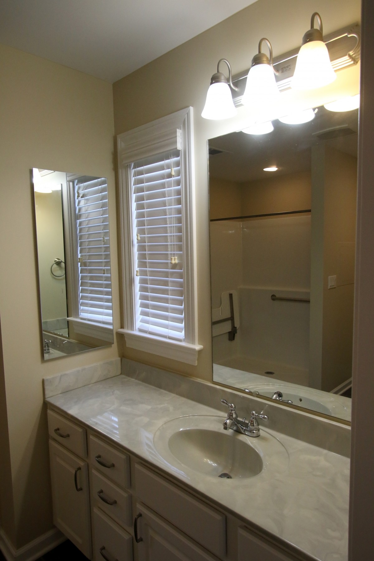 A clean and modern bathroom features a large mirror, marble countertop, and shower area.