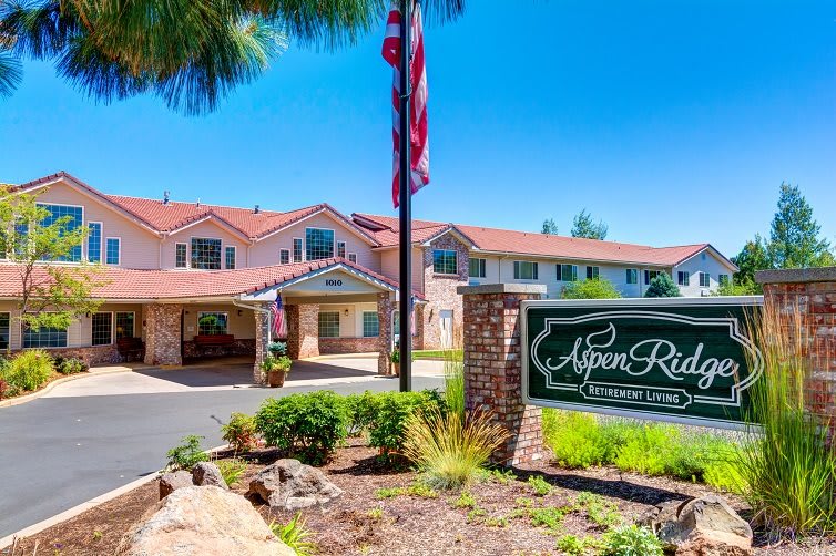 Entrance of Aspen Ridge with a welcome sign and well-maintained landscaping on a sunny day.