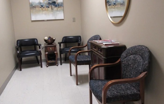 A waiting room with chairs, wall art, and a mirror.