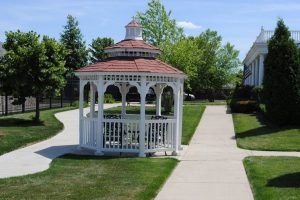A picturesque gazebo in a park setting, surrounded by green grass and trees with a clear blue sky overhead.