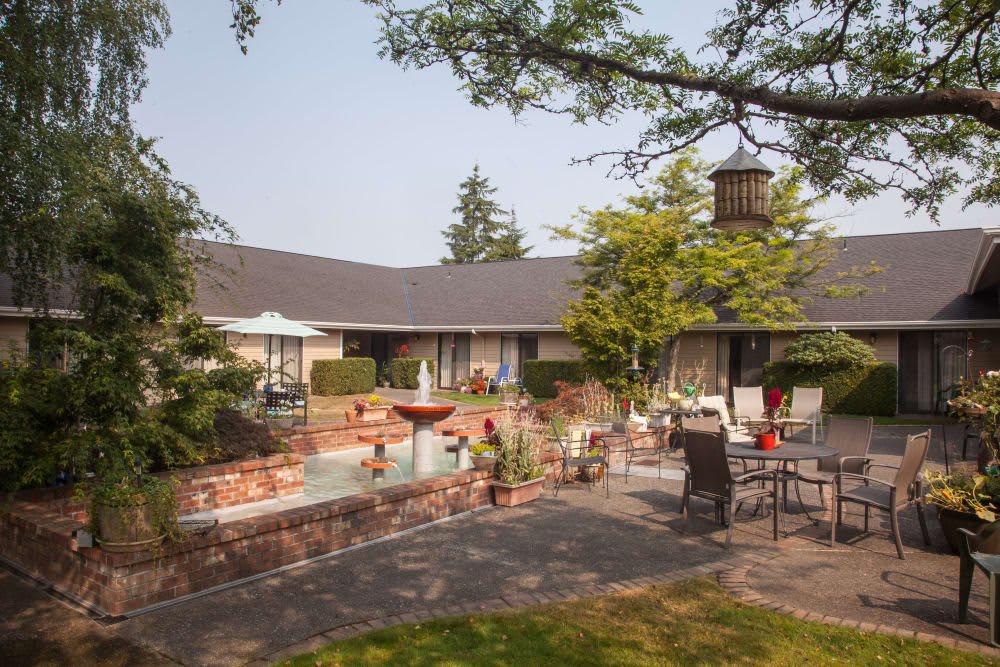 A tranquil courtyard with a fountain, surrounded by tables, chairs, and lush landscaping.