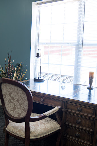A serene workspace featuring a wooden desk and an upholstered chair with natural light streaming in.