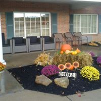 A cozy patio entrance decorated with pumpkins, flowers, and a welcome sign.