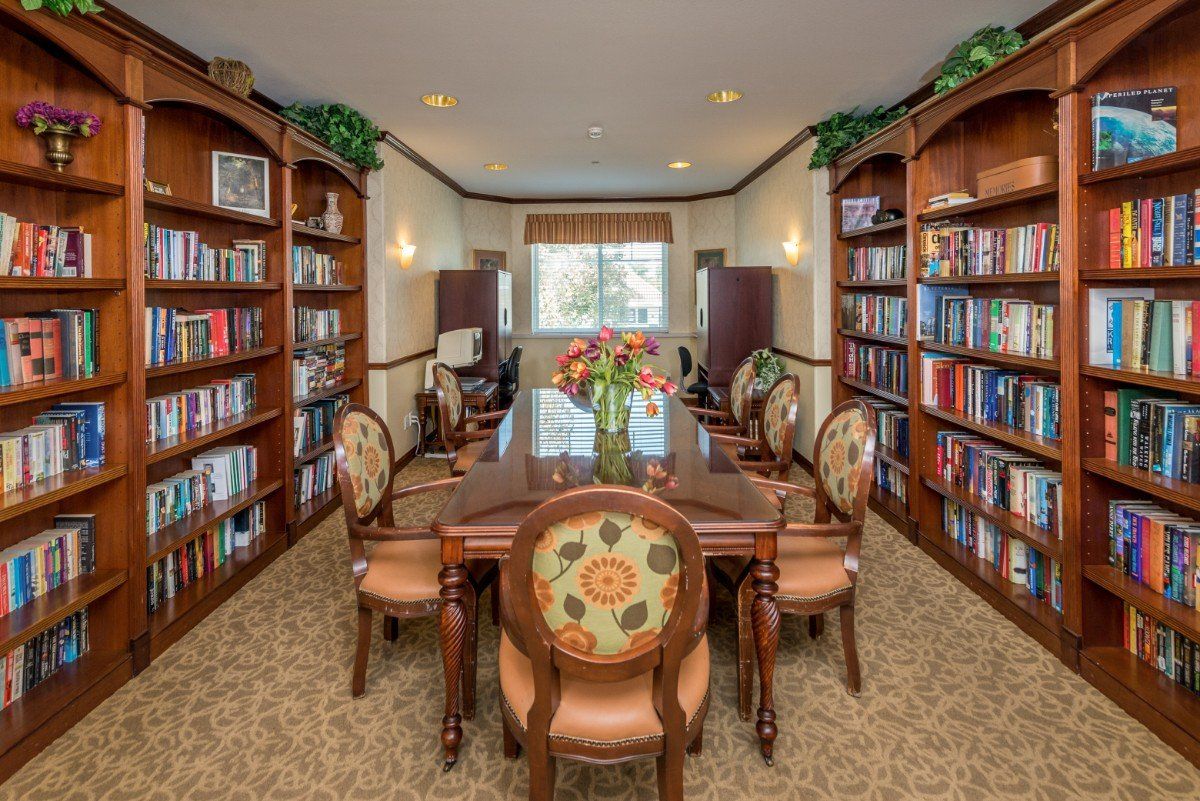 A cozy library room with a large wooden table, elegant chairs, and bookshelves filled with books on either side.