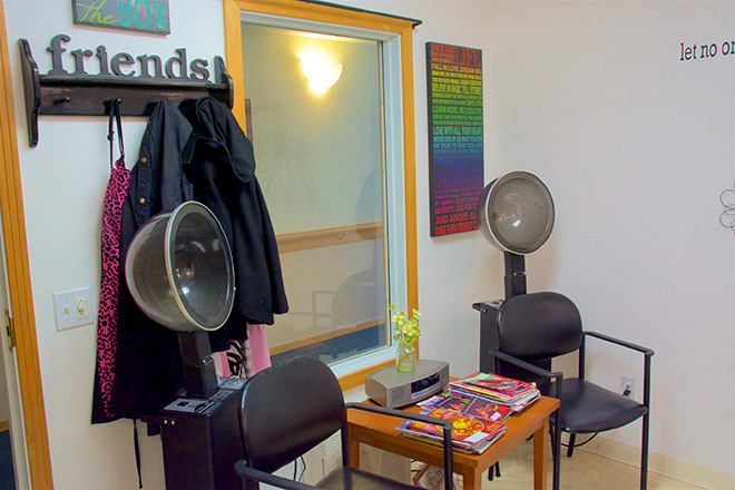 A cozy salon waiting area with hair dryers, chairs, and magazines on a small table.