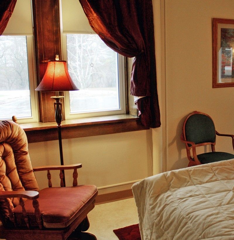 A cozy bedroom interior with a comfortable chair, lamp, and window with curtains.