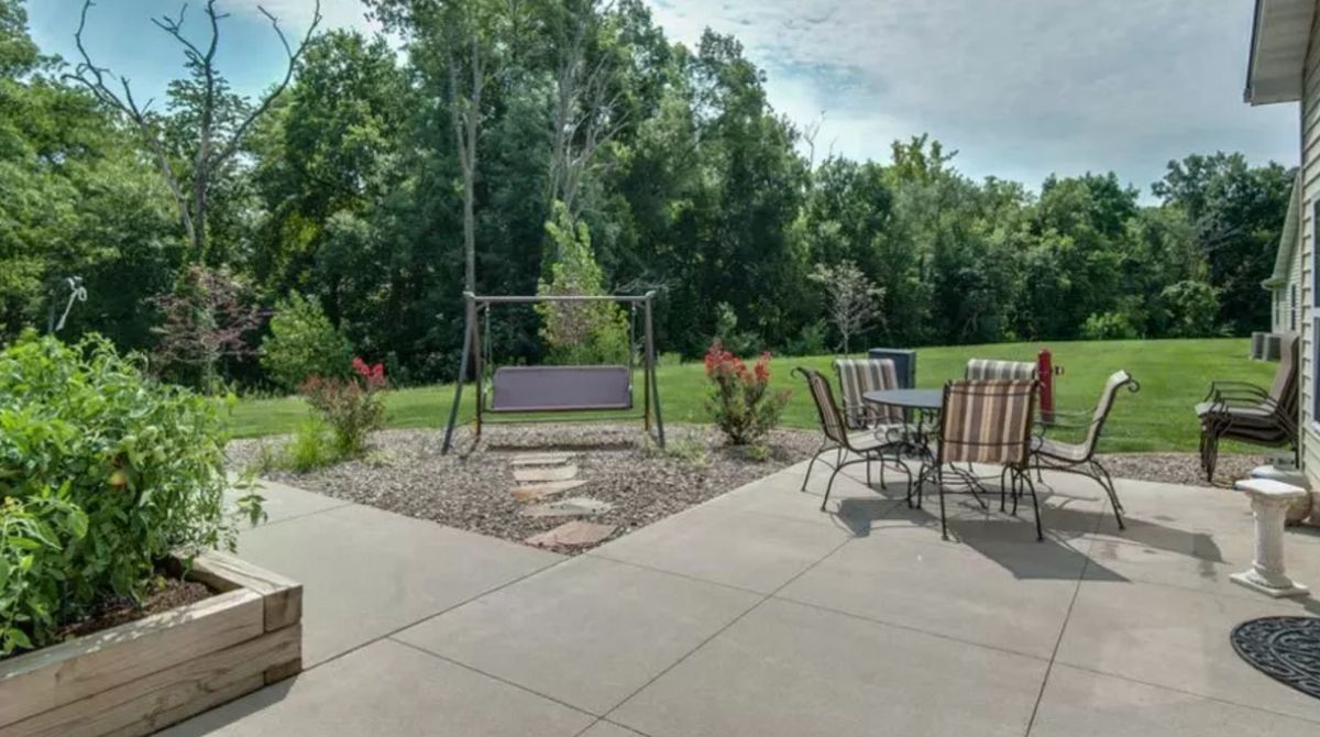 A serene backyard patio with outdoor seating and a swing, surrounded by lush greenery.