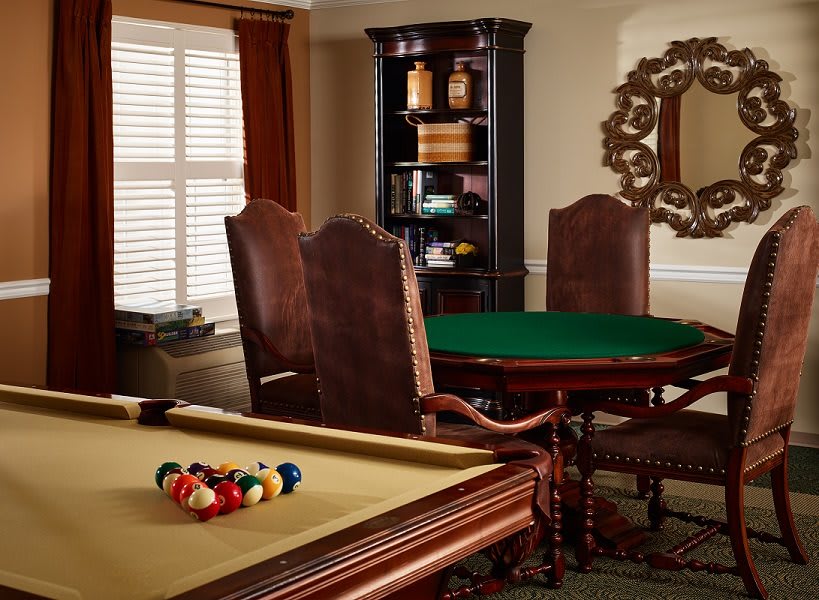 A cozy game room featuring a pool table and a poker table surrounded by leather chairs.