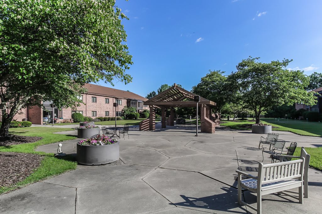 A sunny day in a park with a gazebo, surrounded by benches and trees.