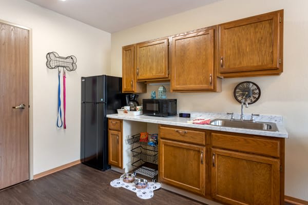A small kitchen area with wooden cabinets, a refrigerator, microwave, and a sink.