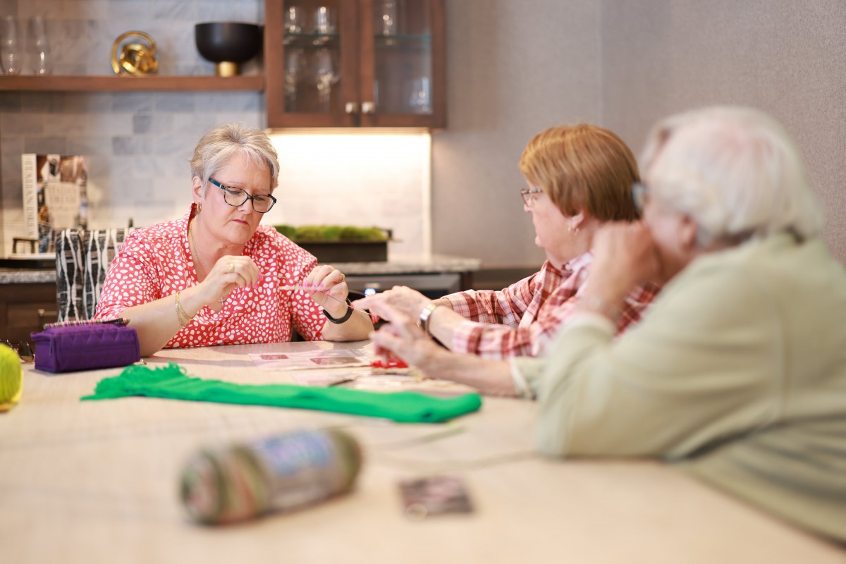 A group of elderly people knitting and socializing together indoors.