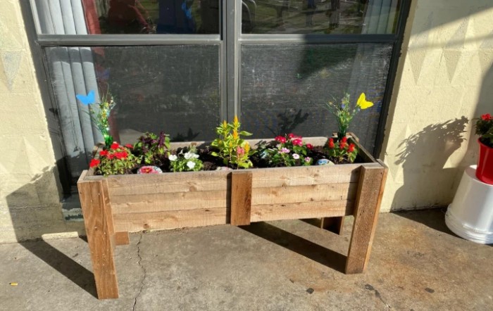 A wooden planter filled with colorful flowers, placed on an outdoor patio.