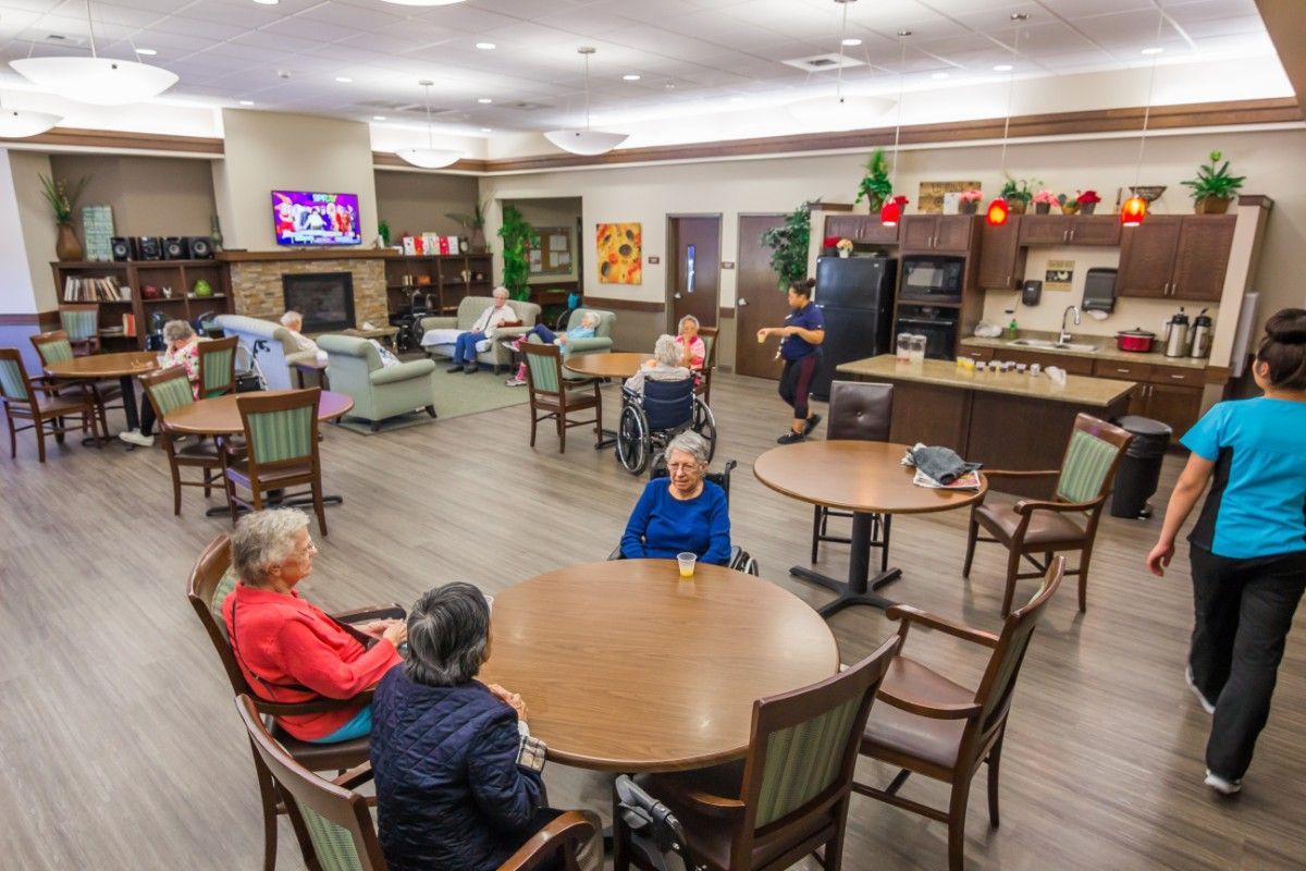 A community room in a senior living facility where elderly residents are socializing around tables.