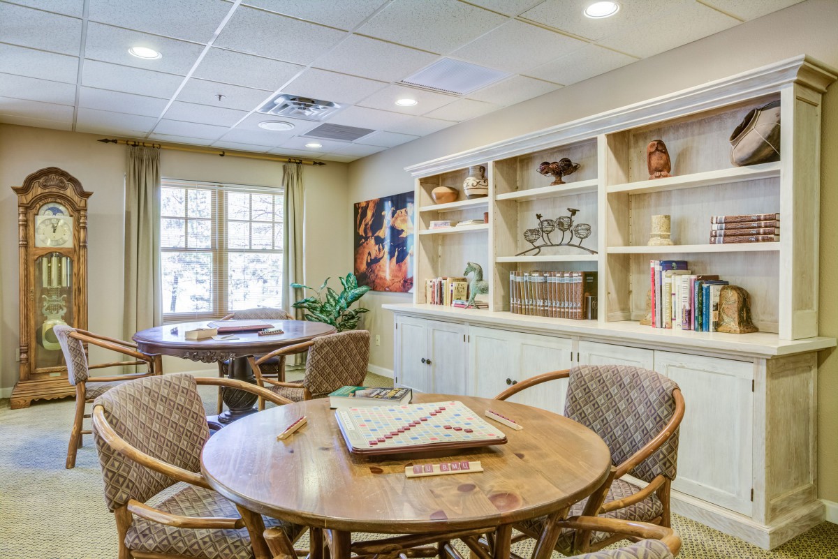 A cozy reading room with wooden tables and chairs, surrounded by bookshelves filled with books and decorative items.