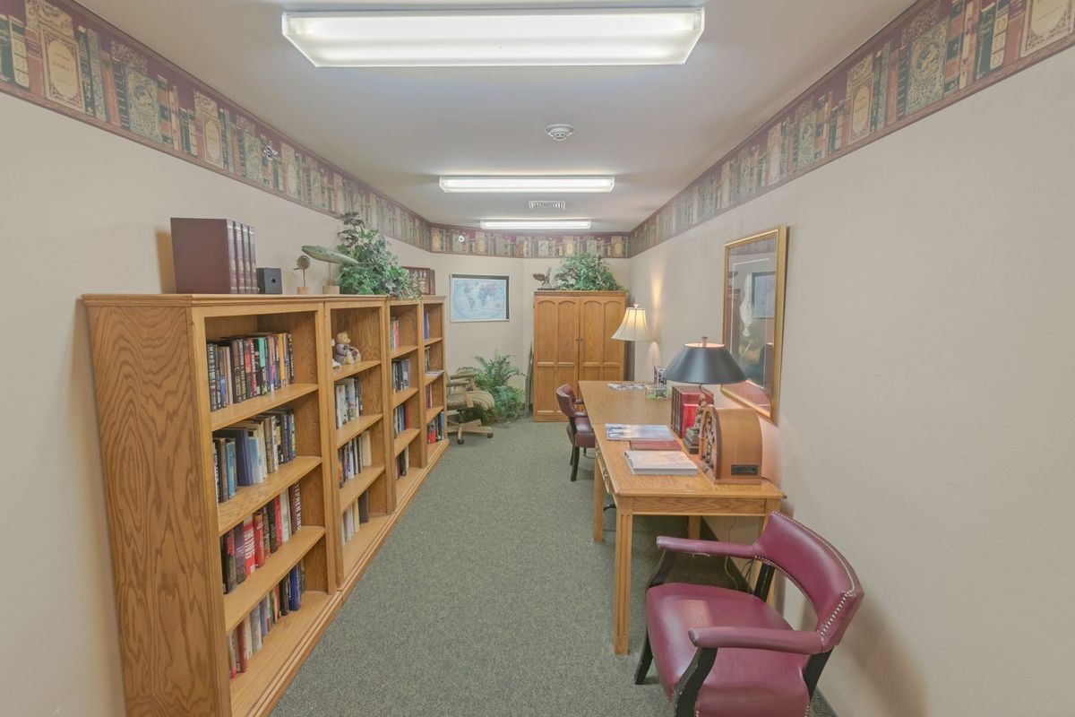 A quiet library room with bookshelves lining the walls, tables and chairs for reading.