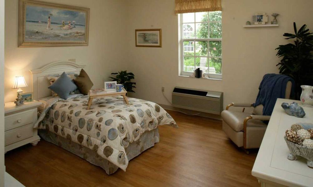 A cozy bedroom with a neatly made bed, featuring a decorative comforter, a window offering natural light, and comfortable seating.